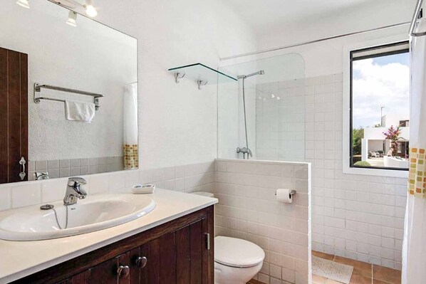 A modern bathroom with a white sink, dark wooden vanity, a glass shower enclosure, and a white toilet.