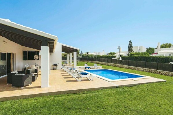 A modern outdoor pool area with lounge chairs and a covered seating area.