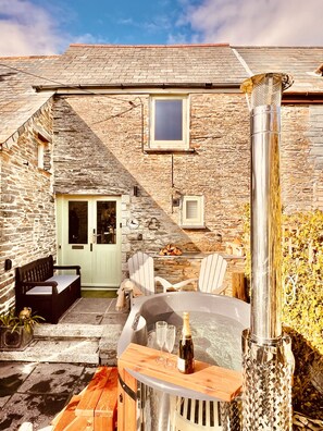 A stone building with a wooden deck, outdoor seating, and a hot tub.