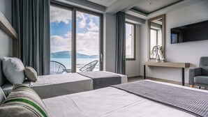 Una habitación de hotel moderna con una cama grande, una zona de estar con vistas al mar, un televisor de pantalla plana y una pequeña mesa con adornos.