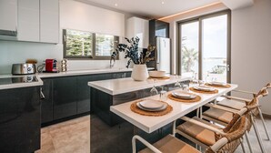 Una cocina moderna con armarios oscuros, una encimera blanca y un comedor con una mesa dispuesta para cuatro comensales.