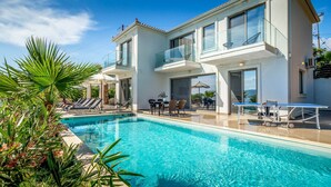 Una casa moderna de dos pisos con piscina, mobiliario exterior y mesa de tenis.