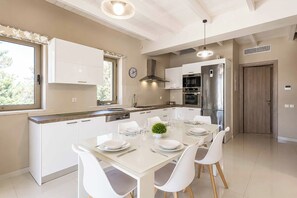 A modern kitchen with white cabinetry, a dining table set for four, and a large window.