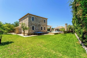 A stone house with a patio, a swimming pool, and a well-maintained lawn.