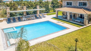 Una piscina con sillas de descanso, un porche cubierto y una casa de piedra con techo de tejas.