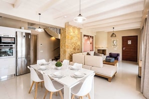 A modern kitchen with a stainless steel refrigerator, a dining table set for four, and a staircase leading to an upper level.