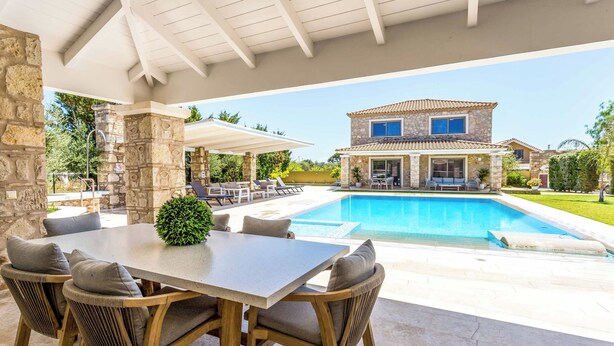 Un patio cubierto con piscina, pilares de piedra y una zona de comedor con sillas y una mesa.