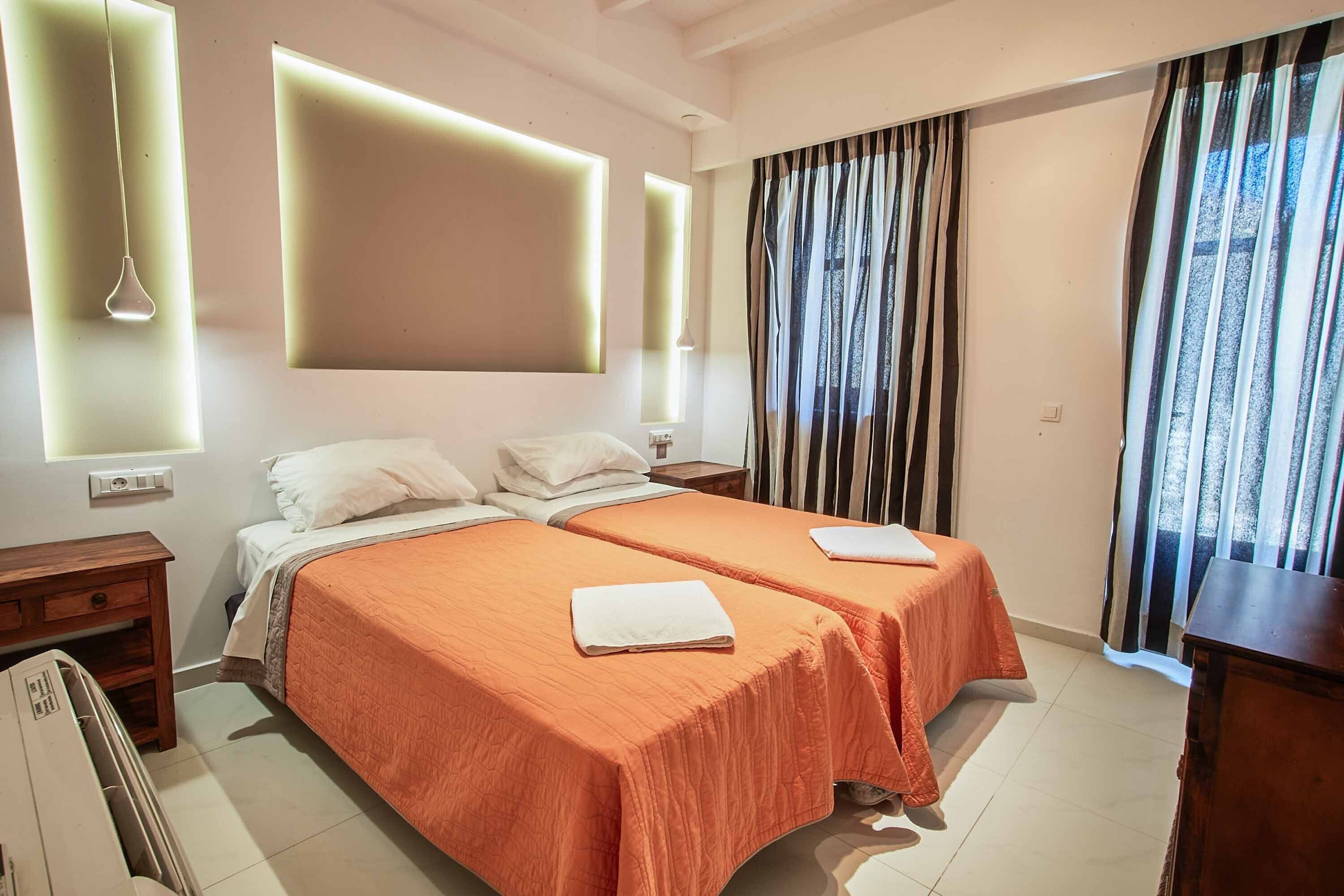 Une chambre d’hôtel avec deux lits, une table de chevet en bois, un bureau et une grande fenêtre avec des rideaux.