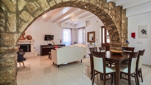Un vaste salon agrémenté d’une arche en pierre, d’une cheminée, d’un canapé, d’une table à manger avec des chaises et d’un téléviseur.