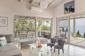 Un vaste espace de vie agrémenté d’une table basse en verre, de canapés gris et d’un balcon offrant une vue sur la mer.