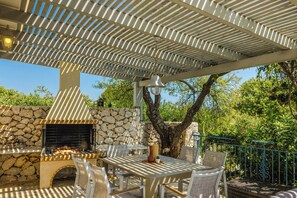 An outdoor patio with a stone fireplace, a table with chairs, and a pergola overhead.