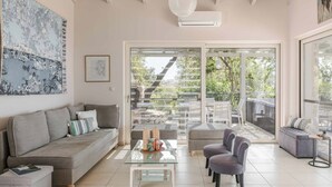 A modern living room with a sofa, armchairs, a glass coffee table, and a sliding glass door leading to an outdoor patio. - Mounda Beach Villa - Four Bedroom Villa, Sleeps 7 (Ionian Islands)