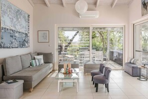 A modern living room with a sofa, armchairs, a glass coffee table, and a sliding glass door leading to an outdoor patio.