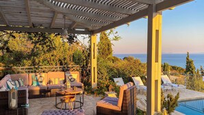 An outdoor seating area with wicker furniture, a stone floor, and a view of the sea. - Mounda Beach Villa - Four Bedroom Villa, Sleeps 7 (Ionian Islands)