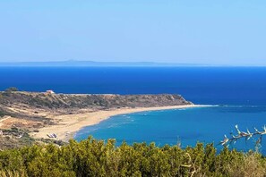 A coastal landscape with a beach, cliffs, and a clear view of the sea.