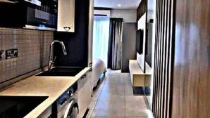 A modern kitchen with a built-in oven, a sink, and a microwave. There is a window with curtains and a flat-screen TV mounted on the wall.