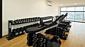 A gym with rows of dumbbells and weight machines, large windows with a city view.