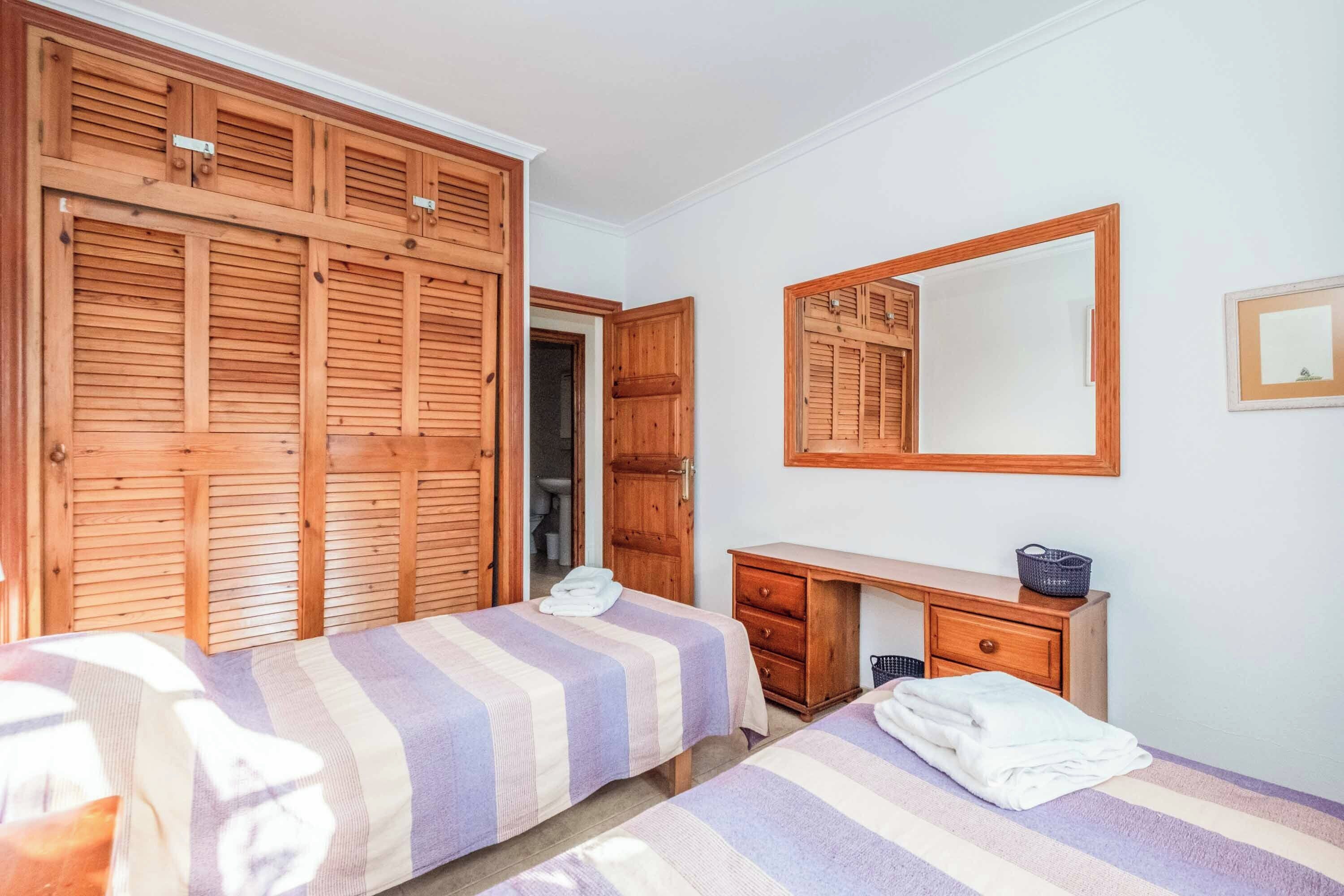 Ein Schlafzimmer mit zwei Betten, einem Holzschrank, einem Spiegel und einem Schreibtisch mit Korb.