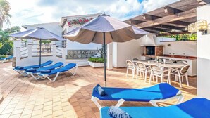 Un espace patio aménagé avec des chaises longues, des parasols et un coin repas doté de sièges extérieurs.