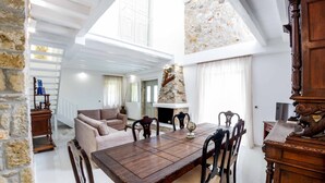 A spacious living area with a high ceiling, a stone wall, a fireplace, and a dining table with chairs.