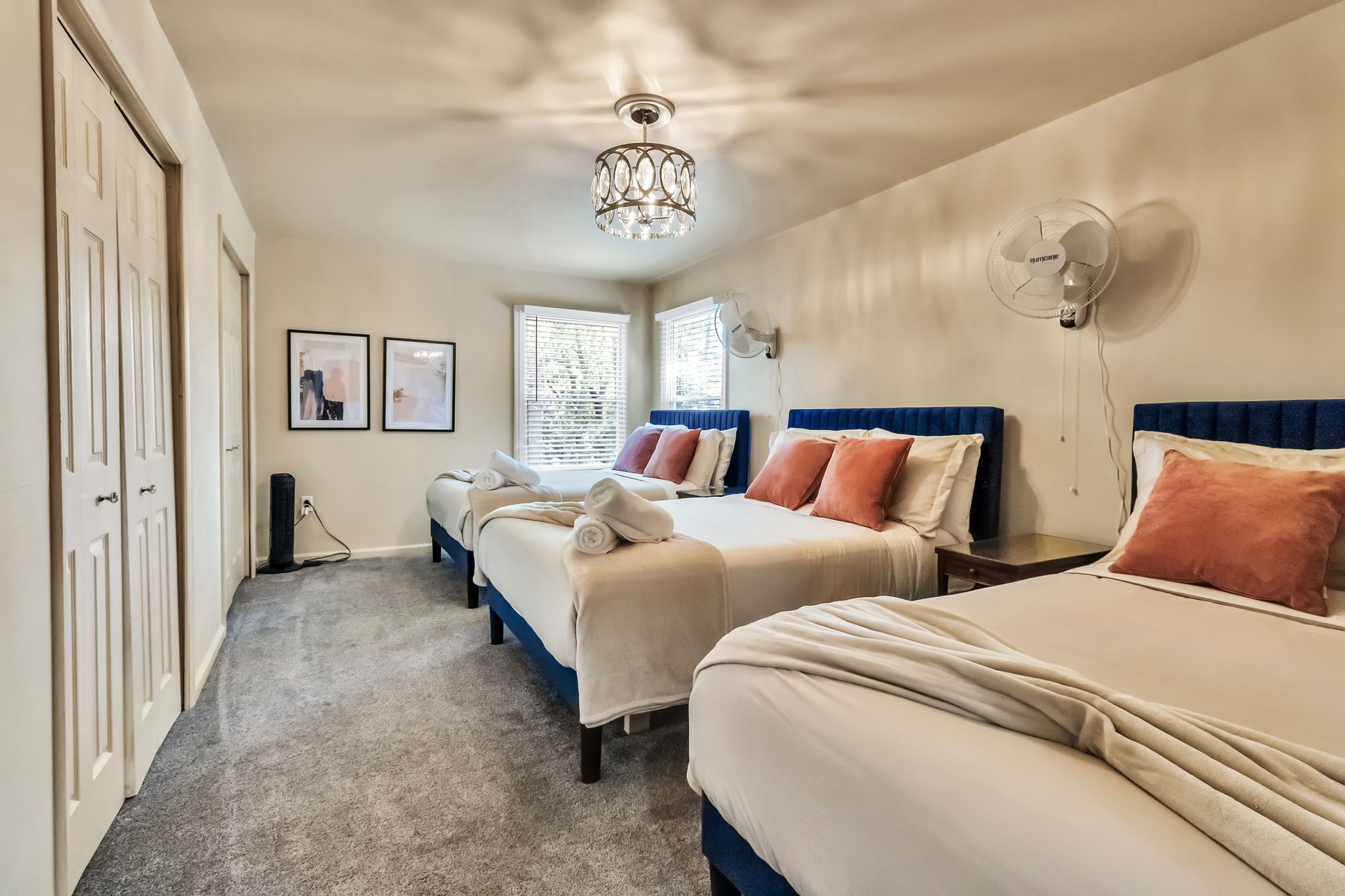 A hotel room with three beds, a chandelier, wall fans, and framed pictures on the wall.