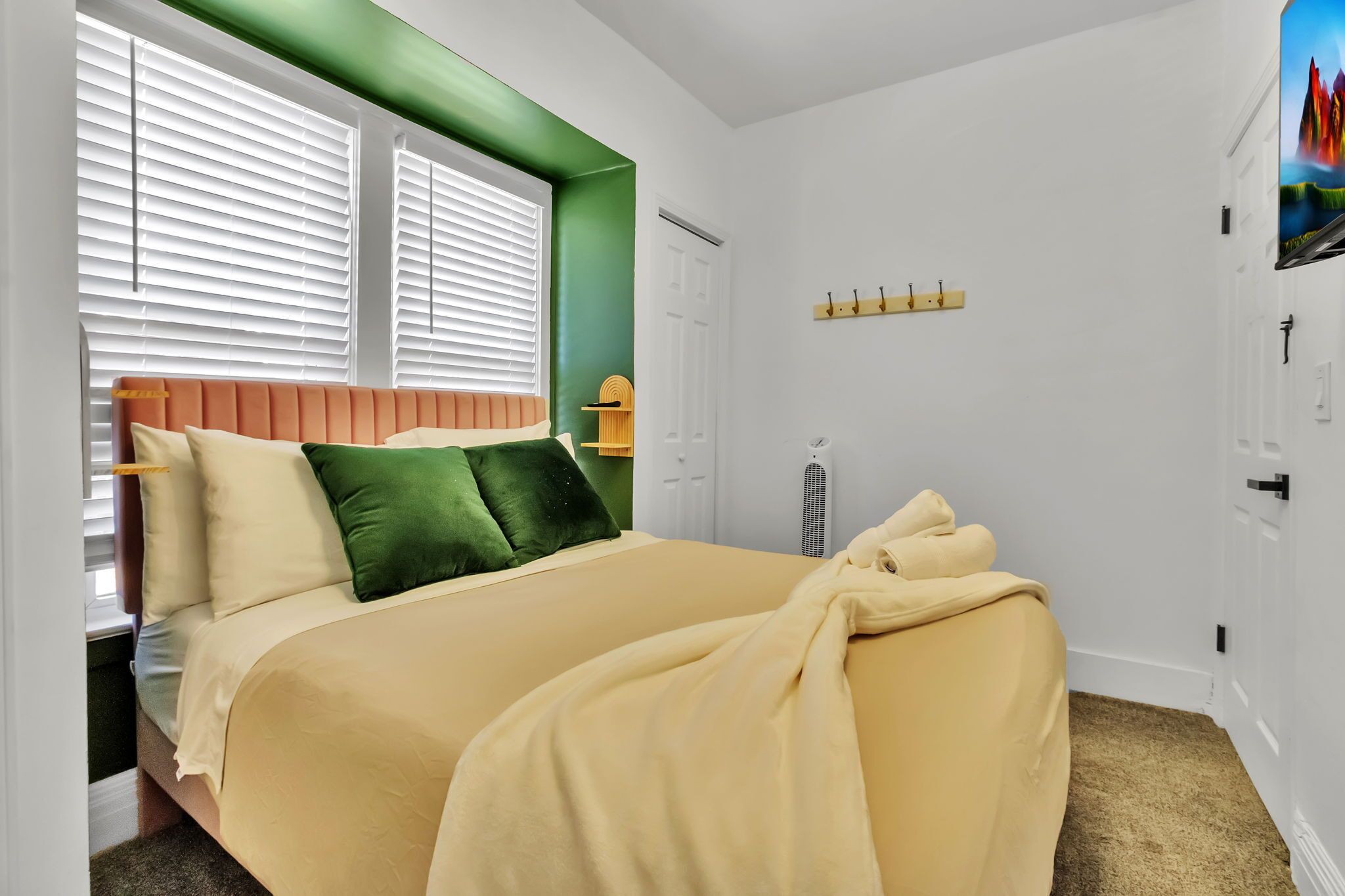 A bedroom with a bed, a window with blinds, a coat rack, and a door.