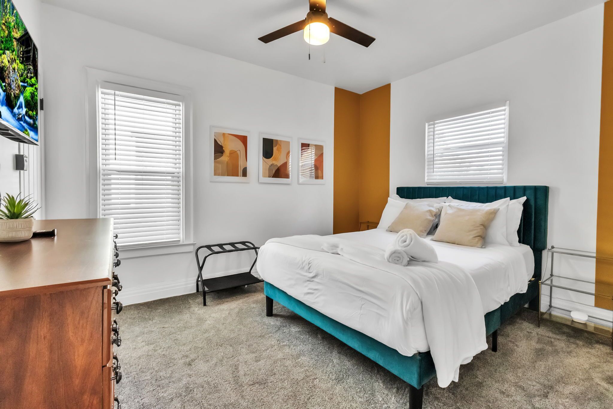 A bedroom with a bed, a ceiling fan, a dresser, and a window with blinds.