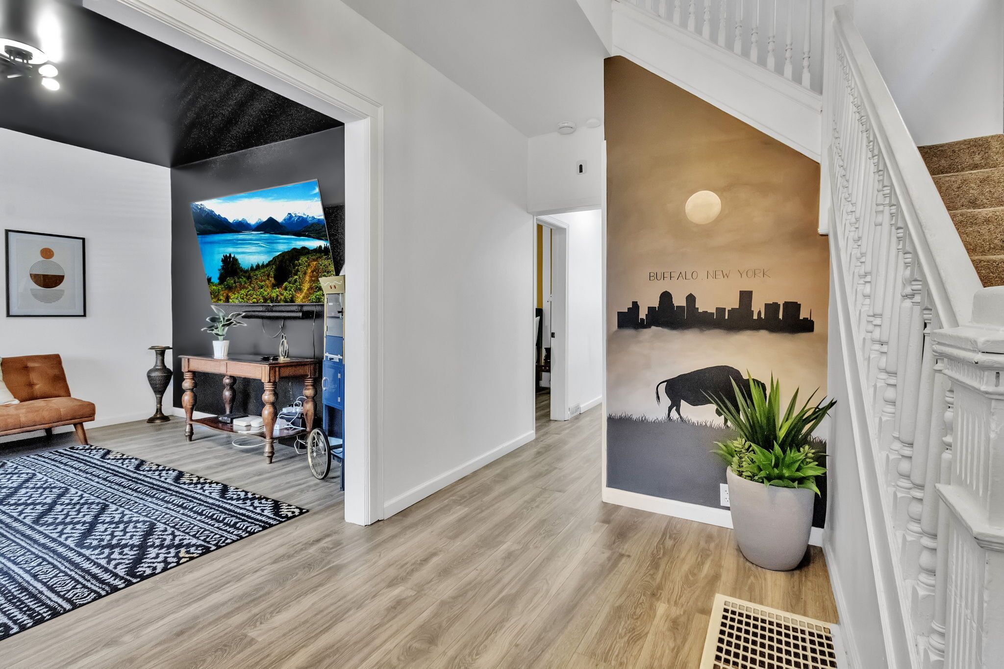 Un intérieur moderne avec un escalier, une fresque représentant un paysage urbain et une vue sur un lac.