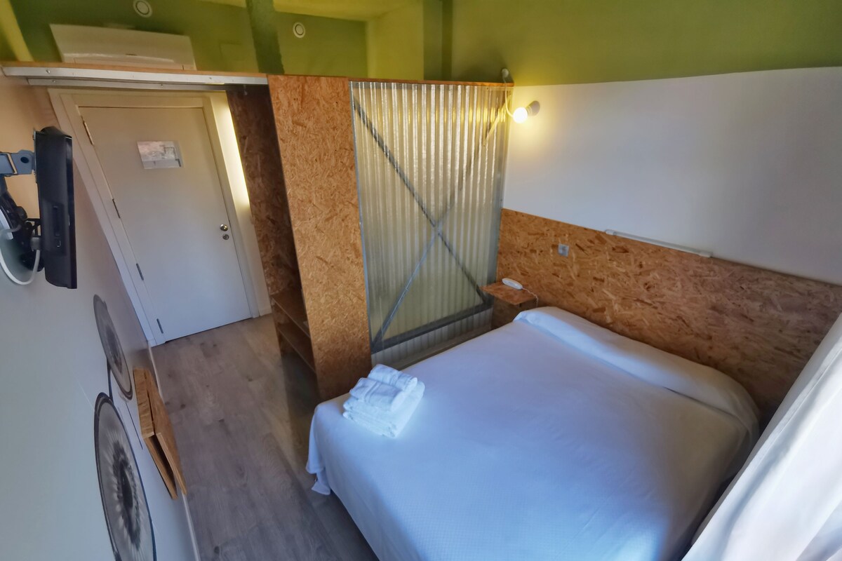 A compact hotel room with a bed, a small table, a mirror, and a door.