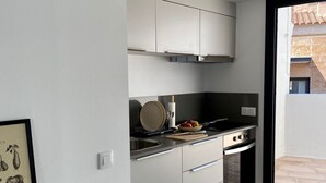 A modern kitchen with white cabinets, a black stove, and a window to the right. - Precioso Ático con Terraza Reformado (Mataró)