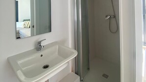 A modern bathroom with a white sink, a mirror, and a glass-enclosed shower. - Precioso Ático con Terraza Reformado (Mataró)