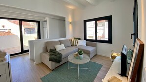 A modern living room with a sofa, a small round table, and a large window. - Precioso Ático con Terraza Reformado (Mataró)