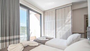 Een moderne hotelkamer met een grote schuifglazen deur die uitkomt op een balkon, een bed met een gestreept bedloper, en een groot raam met gordijnen.