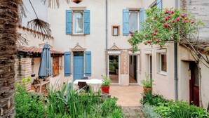Une cour avec une table et des chaises, des plantes en pot et un petit espace aménagé en jardin.