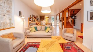 Un vaste espace de vie comprenant un canapé, des fauteuils et une table basse. Un escalier mène à l’étage supérieur.