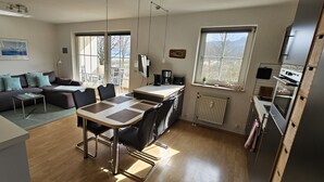 Una cocina moderna con una isla central, un comedor con mesa y sillas, un sofá y un ventanal que proporciona luz natural.