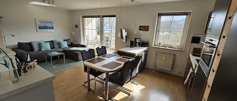 Eine moderne Küche mit Kochinsel, Essbereich mit Tisch und Stühlen, einer Sitzecke und einem großen Fenster für natürliches Licht.