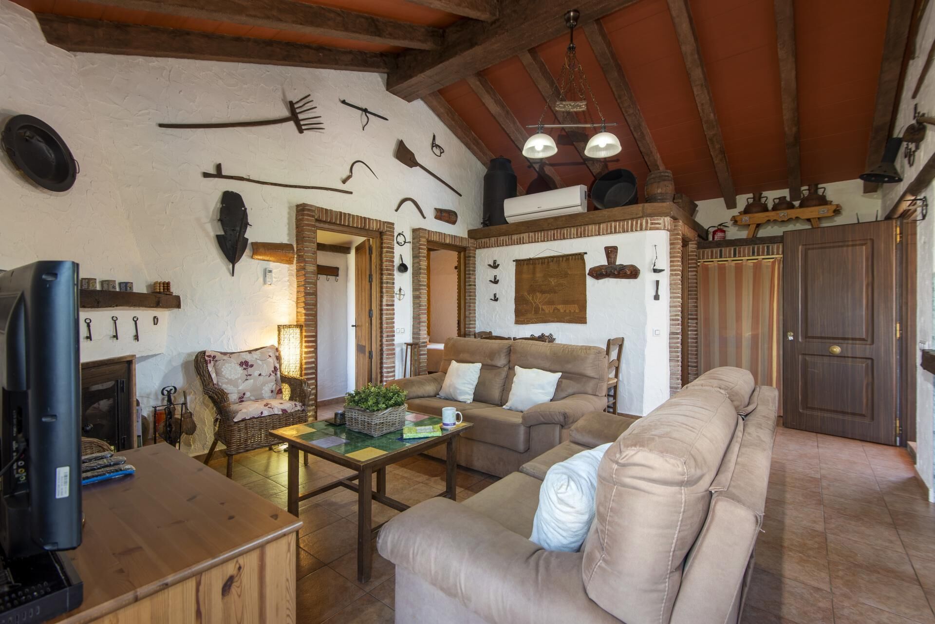 Un salon rustique avec un canapé, une table basse et un téléviseur. Divers ustensiles de cuisine et objets de décoration sont accrochés aux murs.