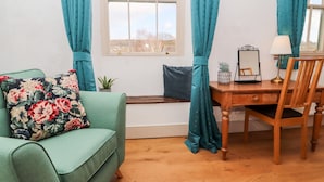 A room with a green sofa, a wooden desk, a chair, and a window with curtains. - Natland Hall Cottage (Kendal)