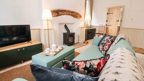 A cozy living room with a flat-screen TV, a fireplace, a sofa, and a coffee table with a tray of tea and biscuits. - Natland Hall Cottage (Kendal)