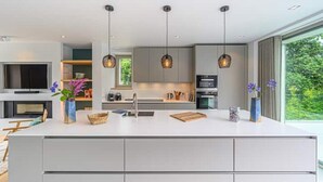 A modern kitchen with a central island, pendant lighting, and a large window offering a view of greenery. - Villa Contemporaine Bord de mer Trinité-sur-mer (La Trinité-sur-Mer)