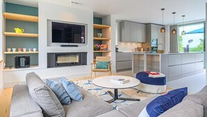 A modern living room with a sofa, a coffee table, and a fireplace. There is a kitchen area with cabinets and a window. - Villa Contemporaine Bord de mer Trinité-sur-mer (La Trinité-sur-Mer)