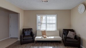 A room with a wooden floor, a white ceiling vent, a window with blinds, and two leather chairs with cushions. - Harris County Ranch Hideaway (Hamilton)