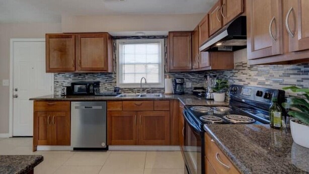 A kitchen with wooden cabinets, a dishwasher, a stove, and a window. - Harris County Ranch Hideaway (Hamilton)