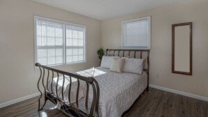 A bedroom with a wooden bed, two windows with blinds, a ceiling light, and a mirror on the wall. - Harris County Ranch Hideaway (Hamilton)