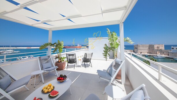 A balcony with white furniture, a fruit bowl, and potted plants.