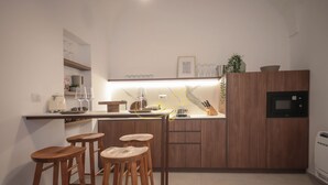 A modern kitchen with wooden bar stools, a built-in microwave, and a countertop with various appliances.