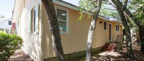 A single-story house with a beige exterior, a front porch, and a small front yard with trees.