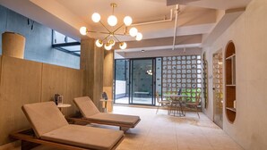 Une salle de spa moderne, dotée de deux fauteuils, d’un luminaire au plafond et d’une porte vitrée donnant sur un espace extérieur.