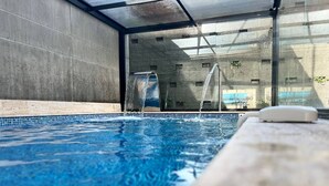 Une piscine intérieure moderne, dotée d’une eau cristalline, d’un toit en verre et offrant une vue sur l’extérieur.